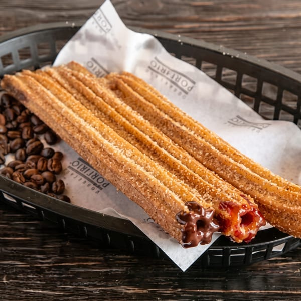 Churros with chocolate and caramel fillings, sprinkled with sugar, served in a black basket with coffee beans.