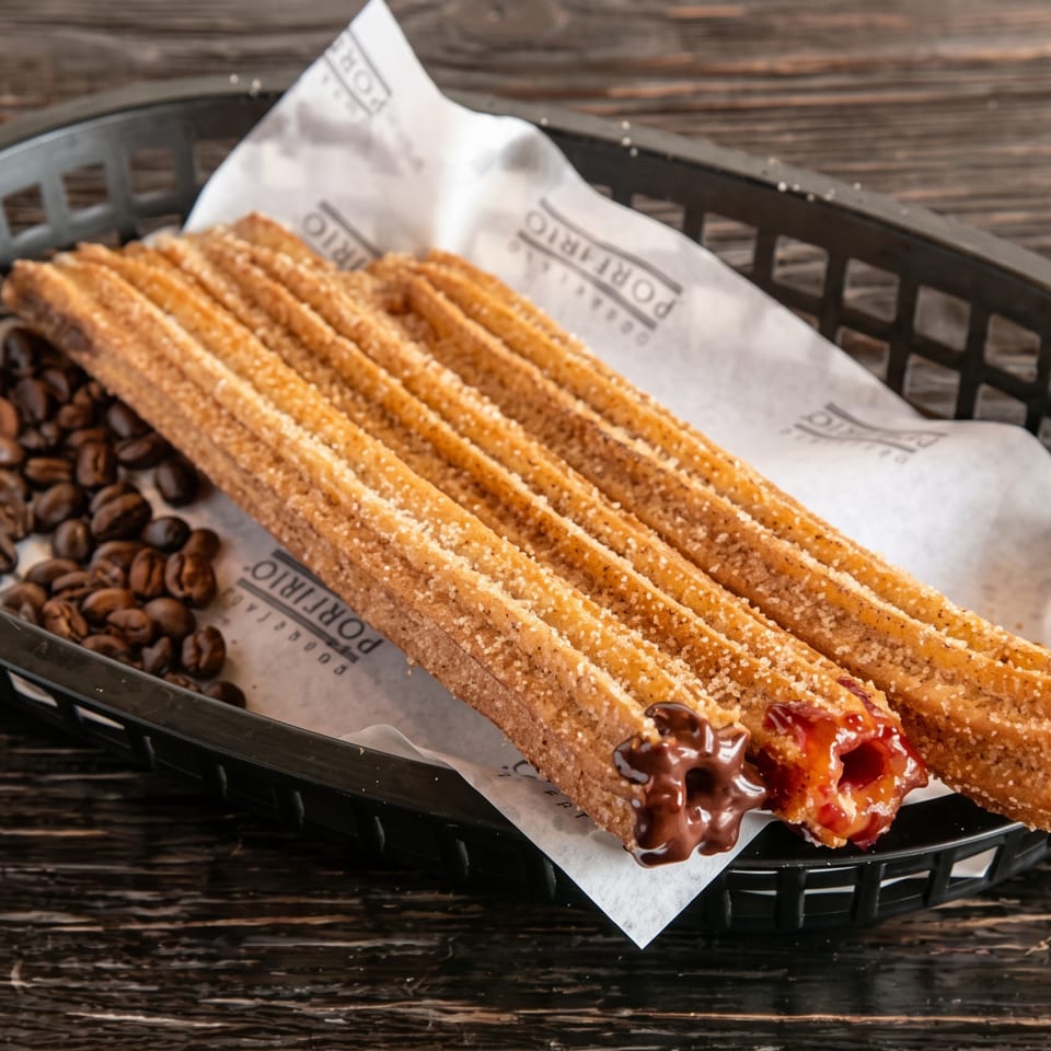 Churros with chocolate and caramel fillings, sprinkled with sugar, served in a black basket with coffee beans.
