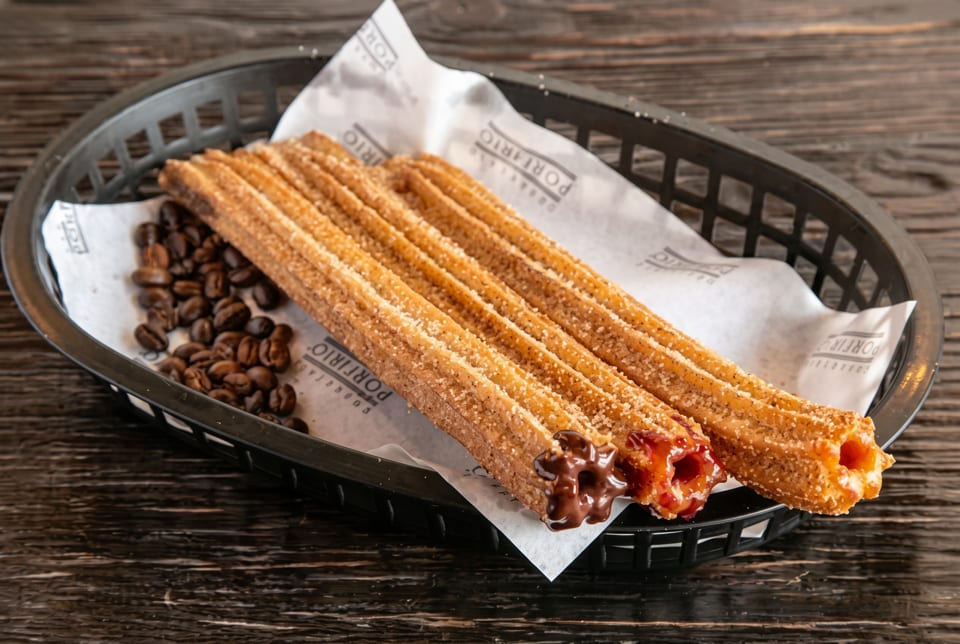 Churros with chocolate and caramel fillings, sprinkled with sugar, served in a black basket with coffee beans.