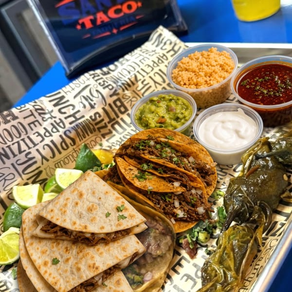 Santo Taco birria tacos, quesadillas, and sides on a tray with a Jarritos pineapple soda.