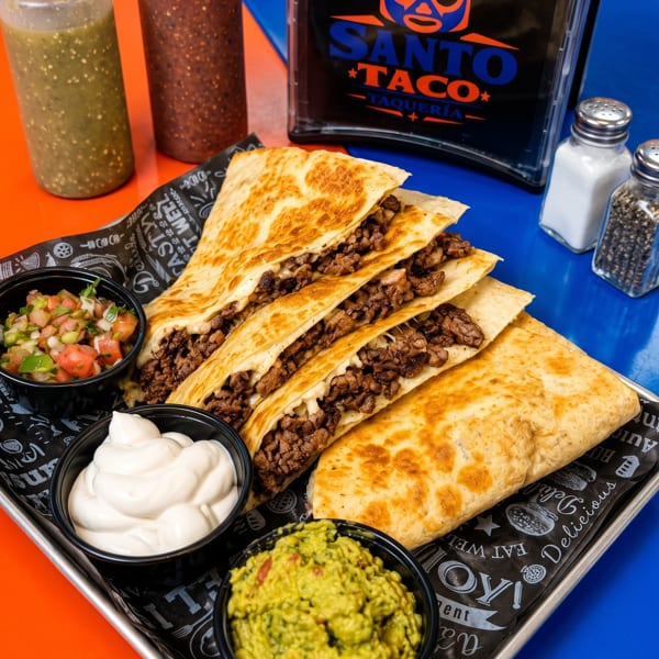 Santo Taco quesadillas with meat, guacamole, pico de gallo, and sour cream on a tray.