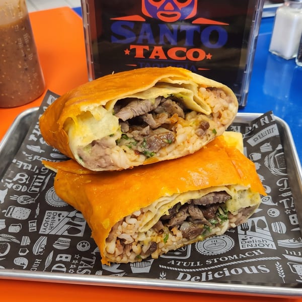 Two large Santo Taco burritos, cut in half, revealing meat and rice filling, on a metal tray.