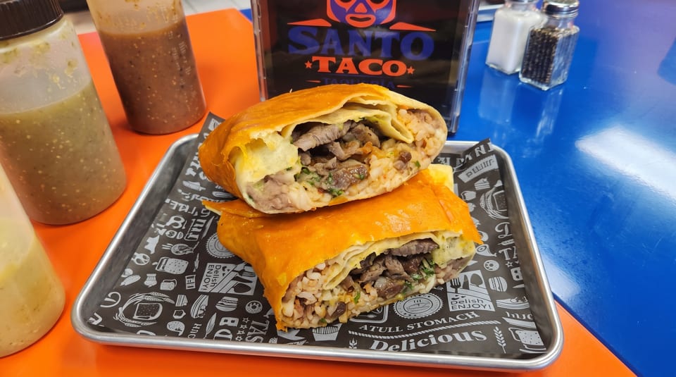 Two large Santo Taco burritos, cut in half, revealing meat and rice filling, on a metal tray.